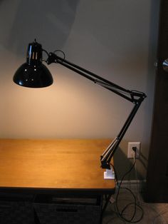 a desk lamp sitting on top of a wooden table next to a light switch and wall