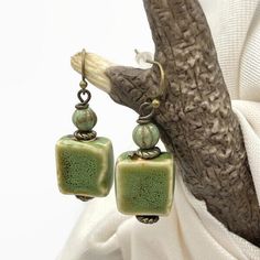 Handmade rustic ceramic beaded earrings. Olive green in color. Smaller in size at 1.5 inches long by .50 inches wide. The square bead is glazed ceramic with a complimenting Czech glass bead at the top. Paired with bronze wires, hooks, and accent beads, these make a perfect casual, rustic style. They would be great for fall. Give them as an affordable gift, or keep them for yourself.  LENGTH: 1.5 inches long WIDTH: .50 wide All of my earrings come with a soft, flexible rubber back that will help Green Bohemian Earrings For Everyday Wear, Green Bohemian Earrings For Everyday, Handmade Rustic Green Earrings, Rustic Green Earrings For Gifting, Rustic Handmade Green Earrings, Artisan Adjustable Green Beaded Earrings, Rustic Green Earrings For Gift, Artisan Green Beaded Earrings Nickel Free, Artisan Green Beaded Earrings As Gift