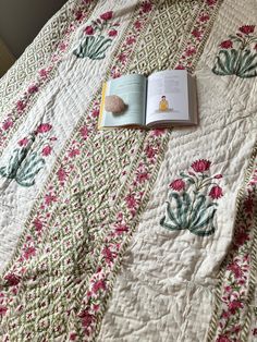 an open book laying on top of a bed next to a flowered bedspread