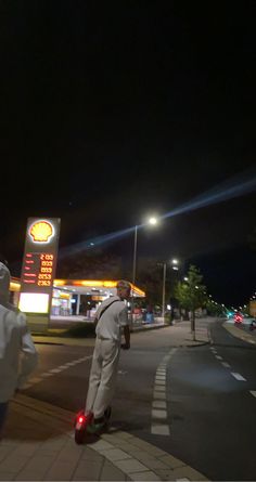 a man riding on the back of a skateboard down a street next to a gas station