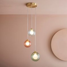 three light fixtures hanging from a ceiling in a pink room with a circular mirror on the wall