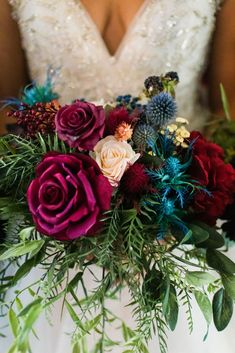 a bride holding a bouquet of red and purple flowers on her wedding day with greenery