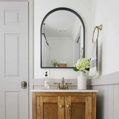 a bathroom vanity with a mirror above it and flowers in a vase on the sink