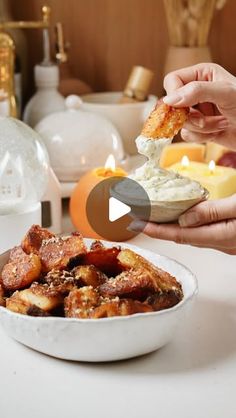 two hands holding food over a bowl on top of a white table with candles in the background