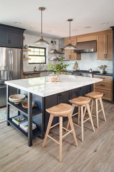 a large kitchen with wooden stools next to an island and stainless steel refrigerator freezer