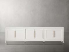 a white sideboard with three doors and two handles on the bottom, in front of a gray wall