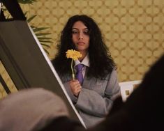 a woman holding a yellow flower in her right hand