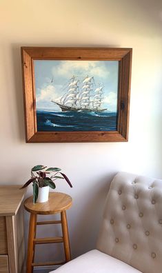 a painting hanging on the wall next to a chair and table with a potted plant