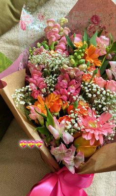 a bouquet of flowers is wrapped in pink and orange paper with a ribbon around it