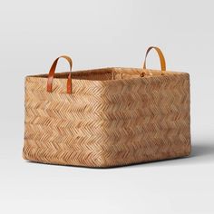 a large woven basket with leather handles on the bottom and sides, sitting in front of a white background