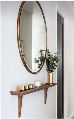 a mirror and some candles on a shelf in a room with white walls, wood flooring and a potted plant