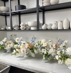 several vases and flowers are arranged on a shelf in front of other white objects