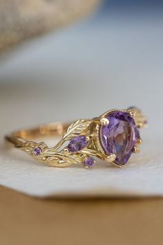 a gold ring with an amethorate and purple stones on it sitting on top of a piece of paper