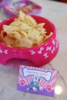 a pink bowl filled with potato chips next to a small sticker that says paw patrol