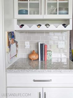 a kitchen with white cabinets and marble counter tops, bookshelf above the sink