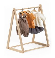 three sweaters are hanging on a wooden rack with clothes in it and one is folded to the side