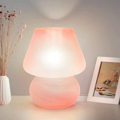 a pink lamp sitting on top of a white table next to a vase with flowers