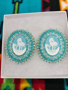 two blue and white earrings with horse silhouettes in the center on a colorful background