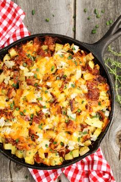 a cast iron skillet filled with cheesy potato casserole on top of a red and white checkered napkin