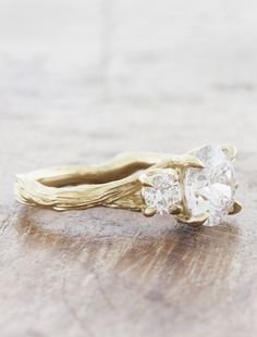 an engagement ring with two round diamonds on the side, sitting on top of a wooden surface