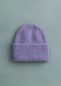 a purple knitted beanie sitting on top of a gray surface next to a green wall