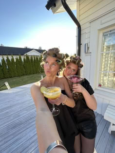 two women are holding drinks and posing for a photo on the deck outside their house