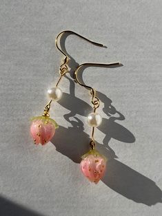 two pink flowers with pearls hanging from gold earwires on a white surface in the sunlight