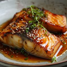 two pieces of fish on a plate with sesame seeds and garnished in sauce