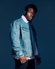 a man in a denim jacket and black pants poses for a photo with his hands on his hips