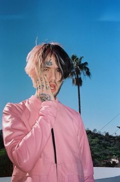 a man with pink hair and tattoos on his face standing next to a palm tree