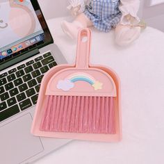 a pink dustpan with a rainbow design on it next to a laptop computer and baby doll