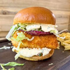 a chicken sandwich with lettuce, tomato and onion on a wooden cutting board