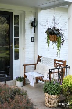 the front porch is decorated with potted plants and hanging planters, along with two chairs