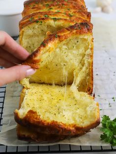 a person holding a piece of bread with cheese on it and sprinkled with parsley