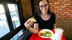 a woman sitting at a table with a plate of food in front of her and a drink