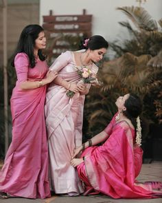 three women in pink dresses standing next to each other and one is holding a flower