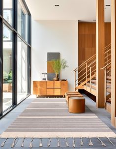 a living room filled with lots of furniture next to tall windows and wooden staircases