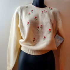 a white sweater with red flowers on it sitting on a mannequin's head