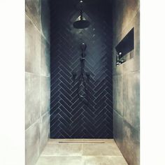 a walk in shower sitting next to a black tiled wall with lights on the side