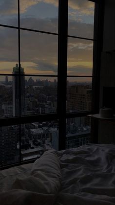 a bed sitting next to a window in a bedroom under a cloudy sky at night