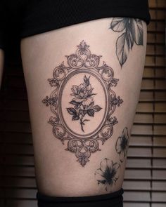 a woman's thigh with tattoos on her legs and flowers in the frame around it