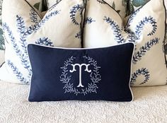 a bed with blue and white pillows on top of it next to a pillow that has the letter m on it