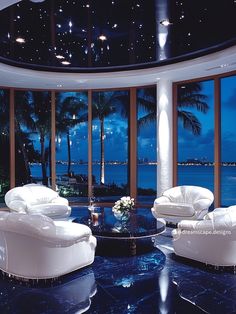 a living room filled with white furniture and large windows overlooking the ocean at night time