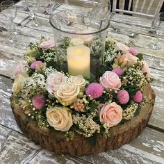 a wooden table topped with a vase filled with pink and white flowers next to a lit candle