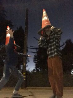 two people standing next to each other with traffic cones on their heads and one person holding his hand up