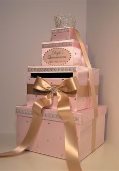 three pink boxes stacked on top of each other with gold ribbons around them and a tiara