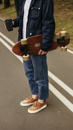 a man is holding a skateboard on the side of the road with two cups in his hand