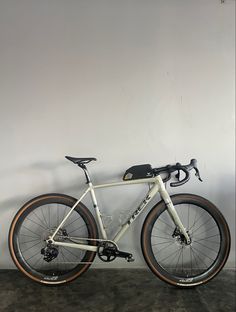 a white bike parked against a wall in front of a gray wall with brown rims