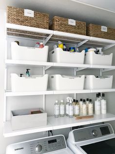 a washer and dryer in a room with white shelves on the wall above them