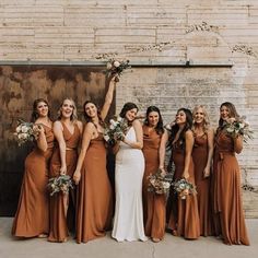 a group of women standing next to each other holding bouquets in front of a brick wall